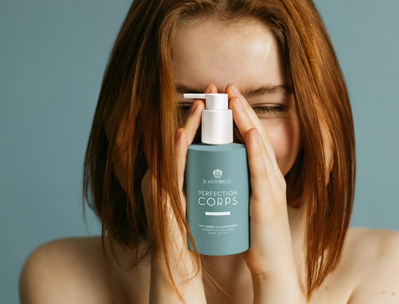 Frau hält die Jean D'Arcel PERFECTION CORPS Body Lotion vor ihr Gesicht und lächelt mit geschlossenen Augen in die Kamera.